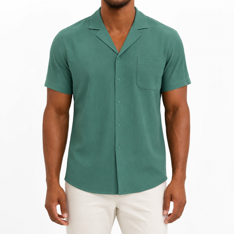 A man wearing a short-sleeve button-up shirt in a muted teal green color, paired with off-white pants, against a plain white background.