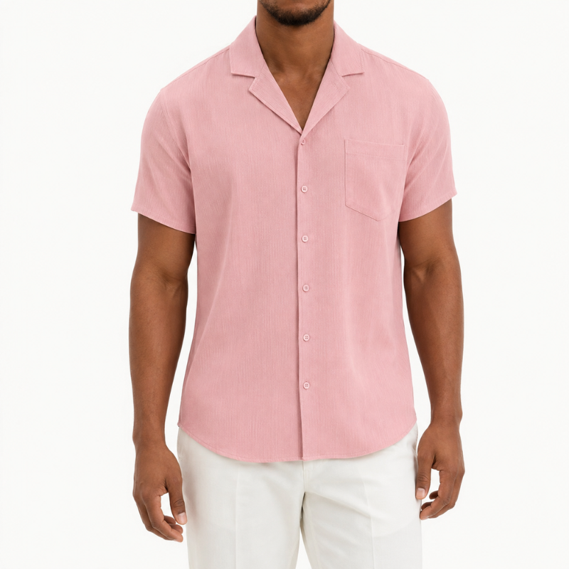 A man wearing a light pink short-sleeve button-up shirt with a collar and chest pocket, paired with white pants, photographed against a clean white background.
