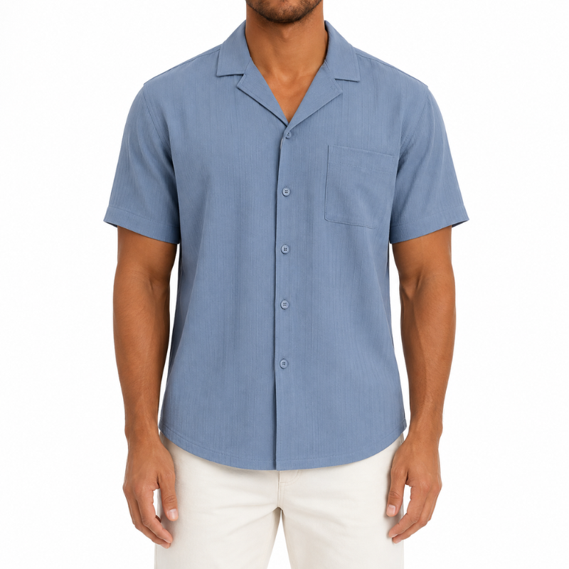 A man wearing a light blue short-sleeve camp collar button-up shirt and white pants, shown from the chin down against a plain white background.