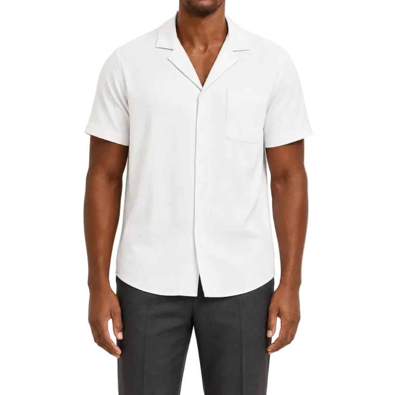 A man wearing a white short-sleeve camp collar button-up shirt and dark gray trousers, shown from the chin down against a light beige studio background.
